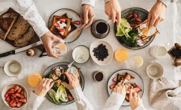 Family having breakfast or brunch together. Flat-lay of French toasts, fried eggs, , bread, orange juice, berries and peoples hands over white table background, top view. People at gathering dinner